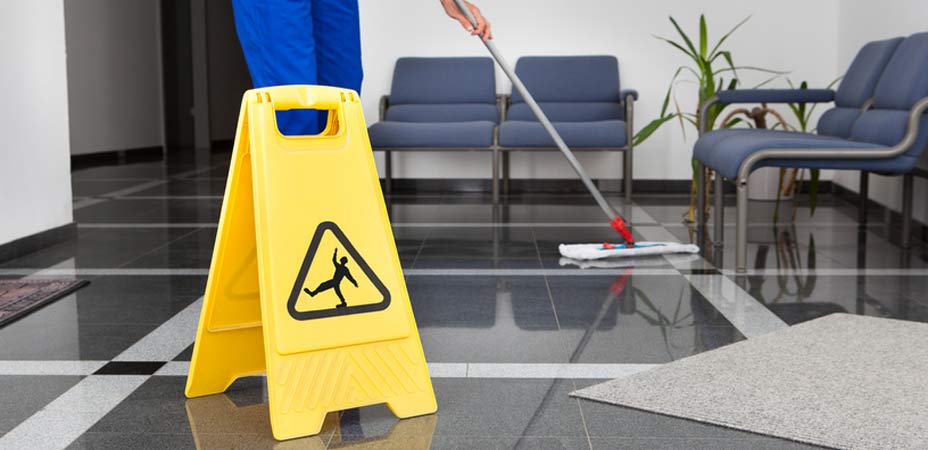 cleaner mopping the floor of an office and a yellow hazard sign in the foreground